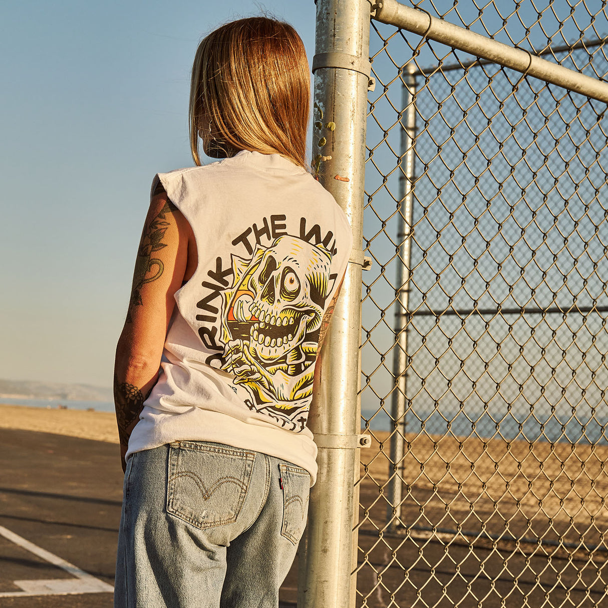 Female model outdoors wearing a sleeveless street tee with 'Drink The Wild Air' graphic