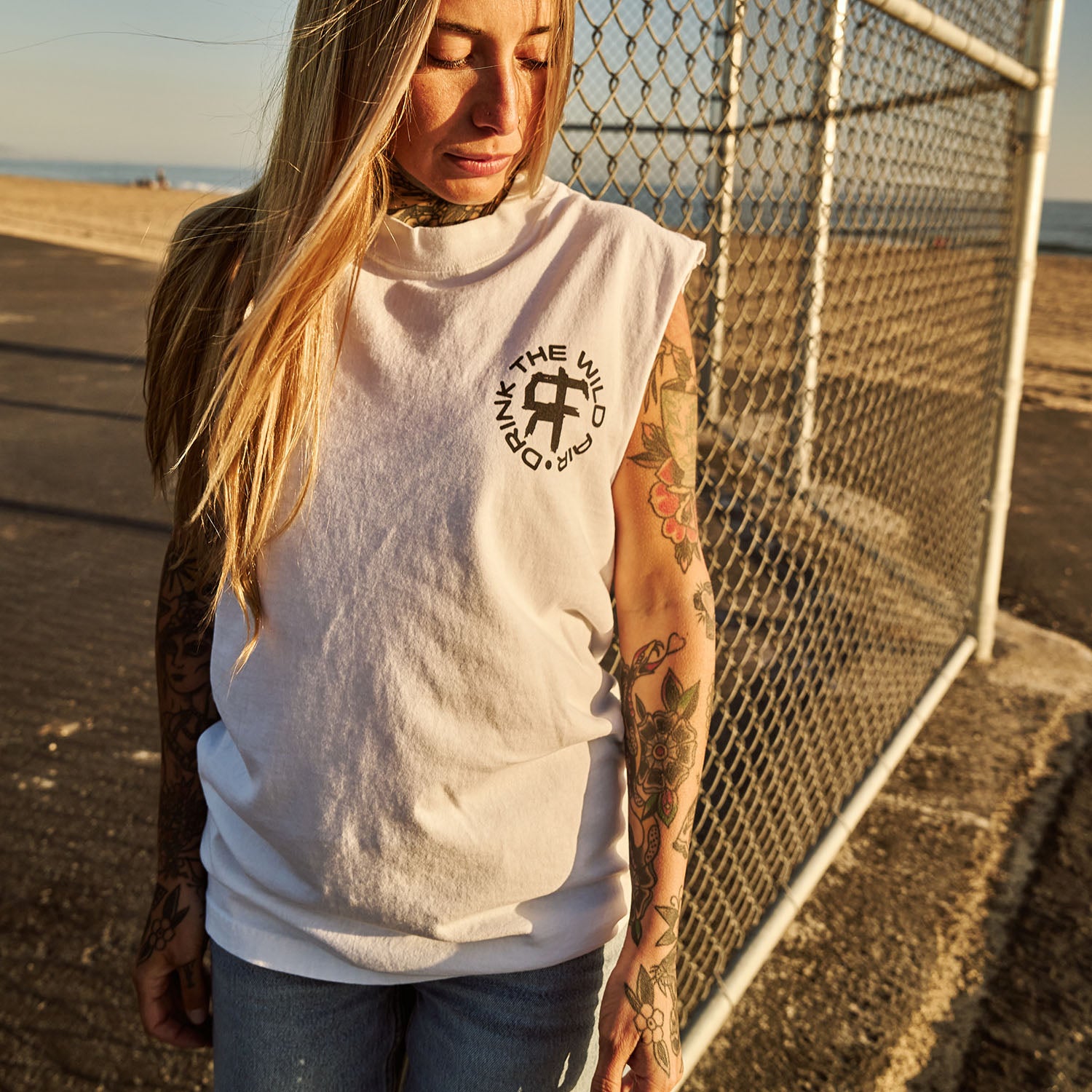 Female model outdoors wearing a sleeveless street tee with 'Drink The Wild Air' graphic