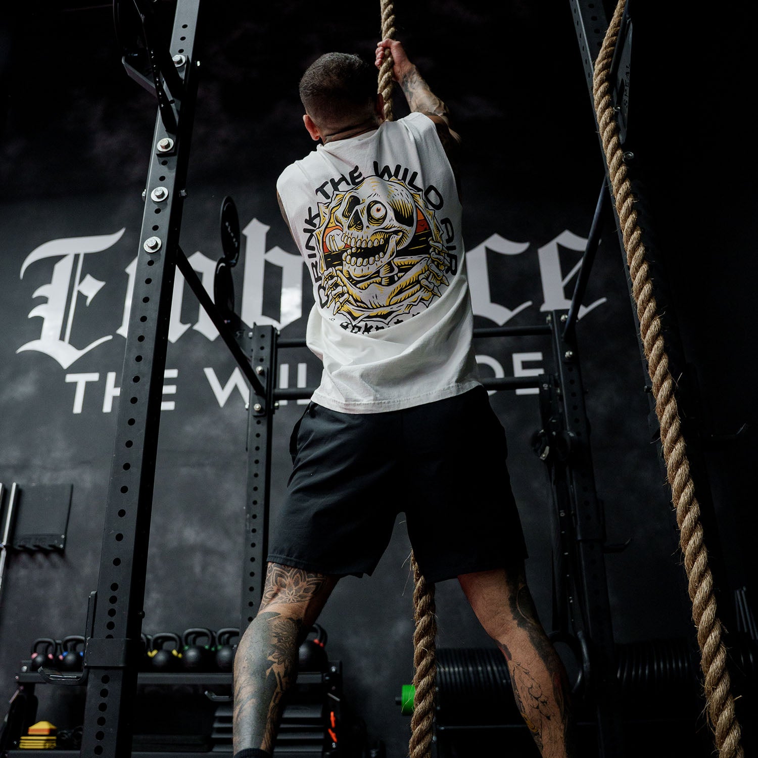 Male model rope climbing in gym wearing the sleeveless street tee with 'Drink The Wild Air' graphic