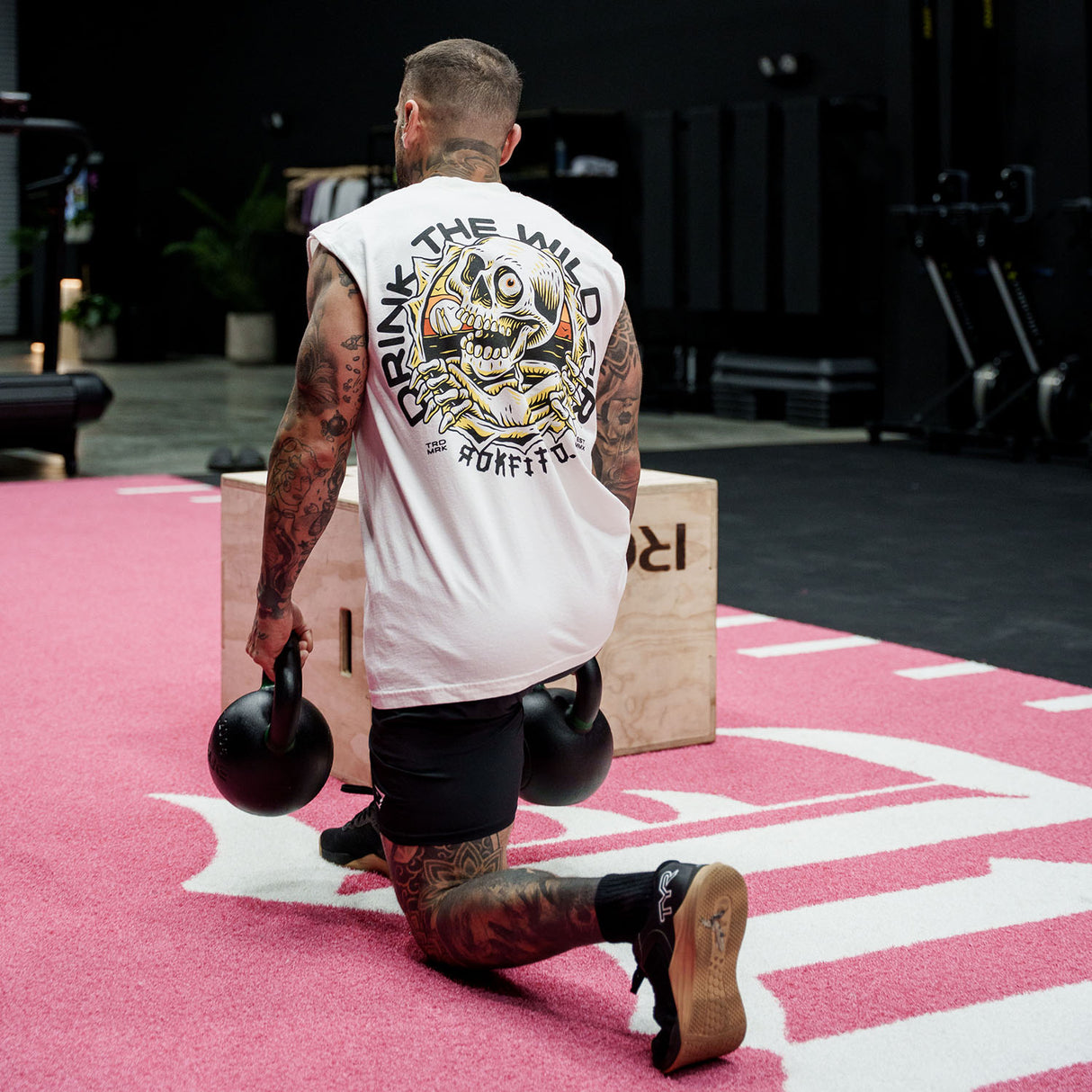 Male model doing a lunge in a gym wearing the sleeveless street tee with 'Drink The Wild Air' graphic