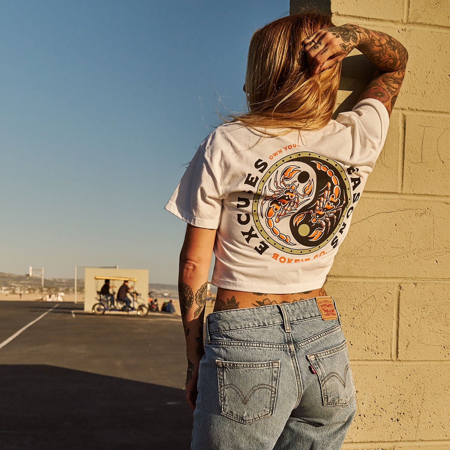 Female model outdoors wearing women's white crop top with 'Excuses or Reasons' graphic