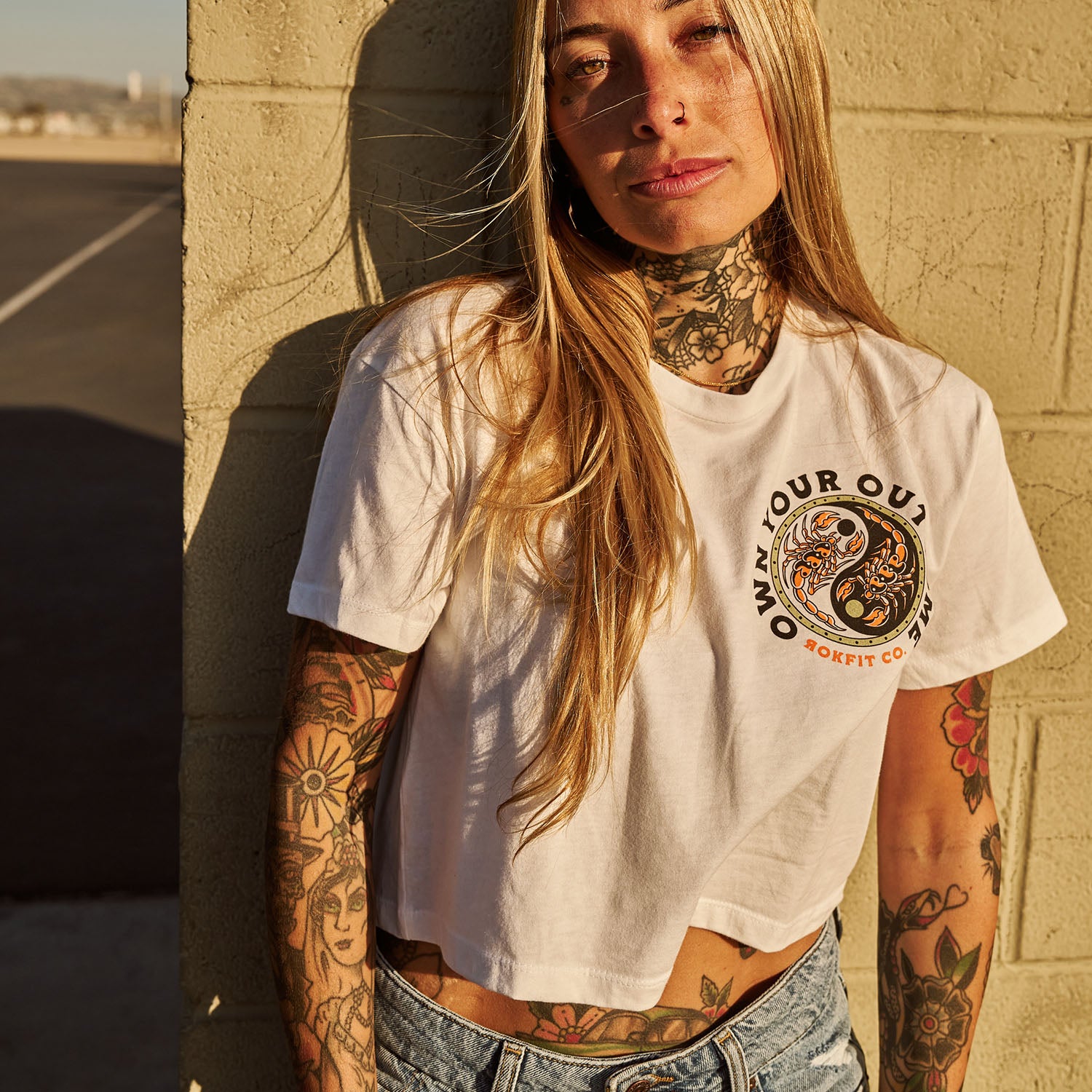 Female model outdoors wearing women's white crop top with 'Excuses or Reasons' graphic
