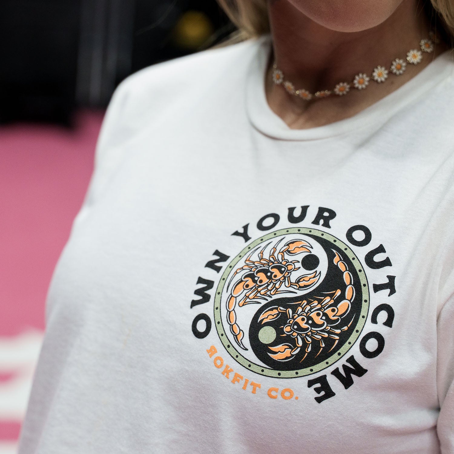 Female model in a gym wearing white crop top with 'Excuses or Reasons' graphic