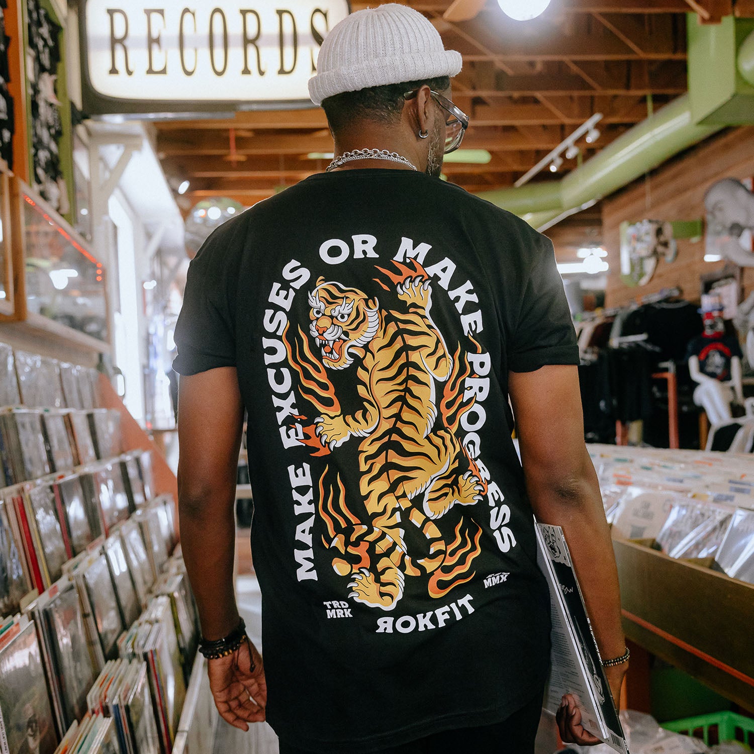 Male model in record store wearing unisex Active Tee with 'Make Excuses or Make Progress' graphic