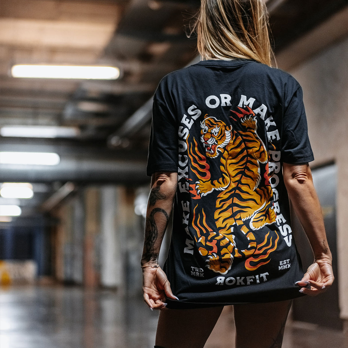 Female model outdoors wearing unisex Active Tee with 'Make Excuses or Make Progress' graphic