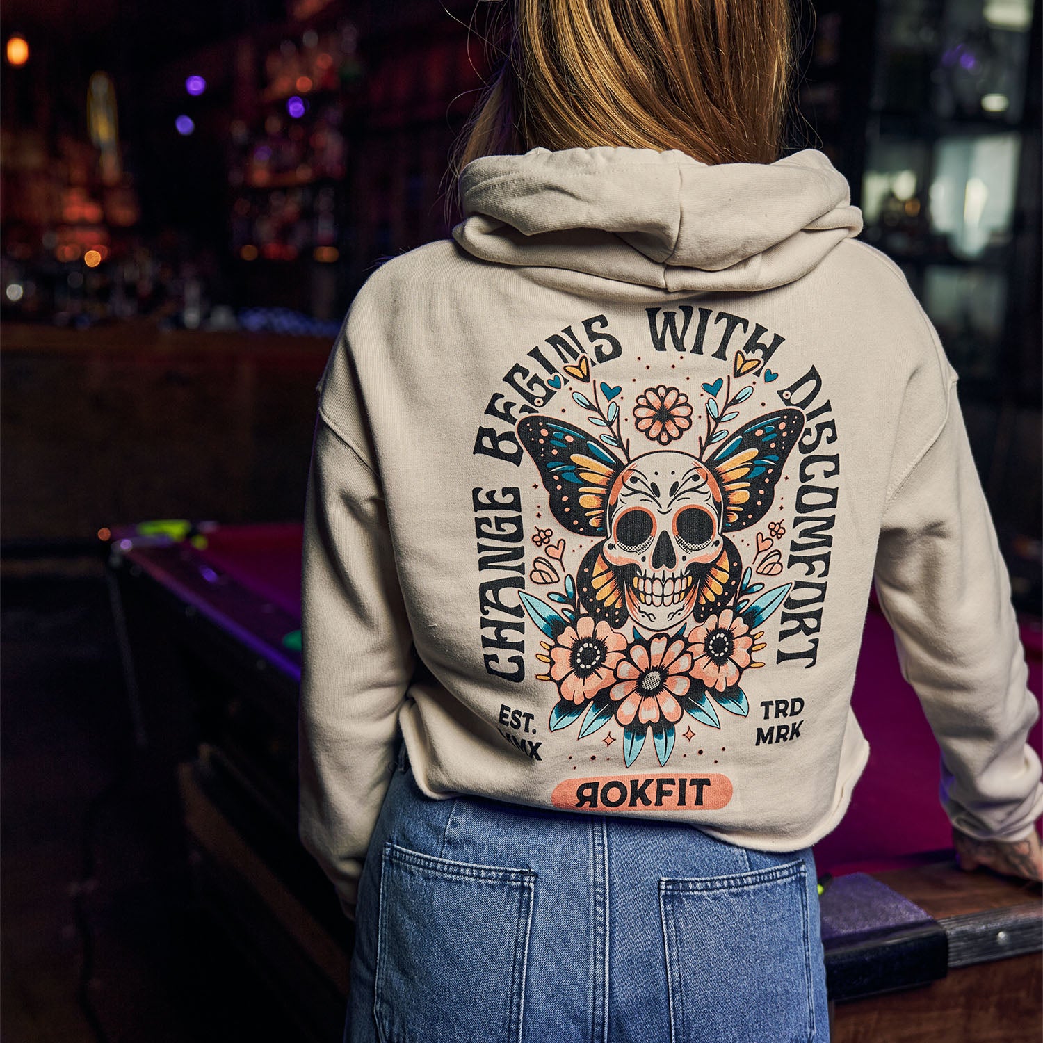 Female model in bar wearing women's Crop Hoody with 'Change Begins With Discomfort' graphic