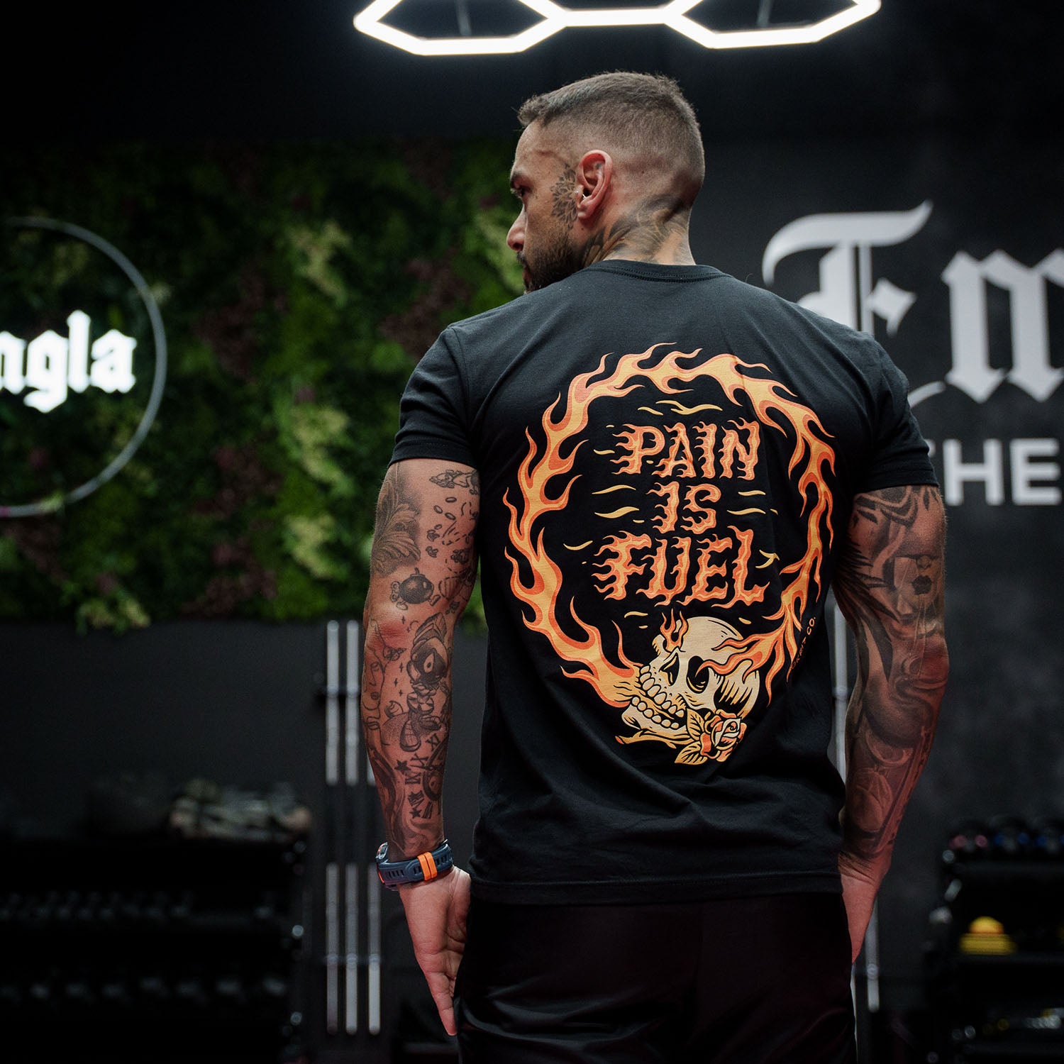 Male model in a gym wearing Active Tee with 'Pain Is Fuel' graphic