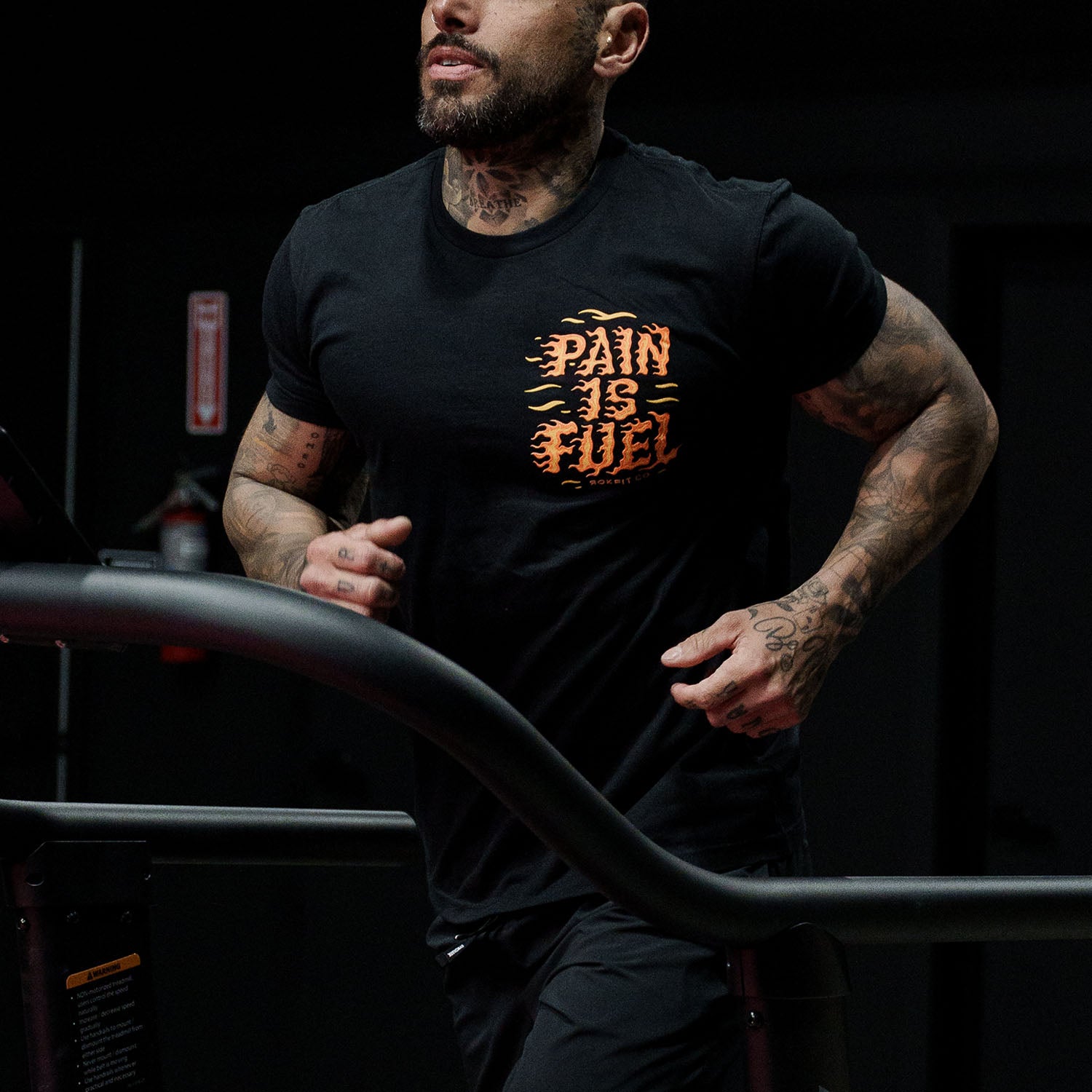 Male model running in a gym wearing Active Tee with 'Pain Is Fuel' graphic