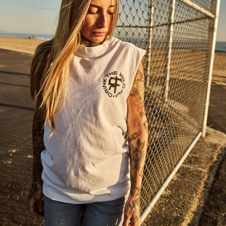 Female model outdoors wearing a sleeveless street tee with 'Drink The Wild Air' graphic