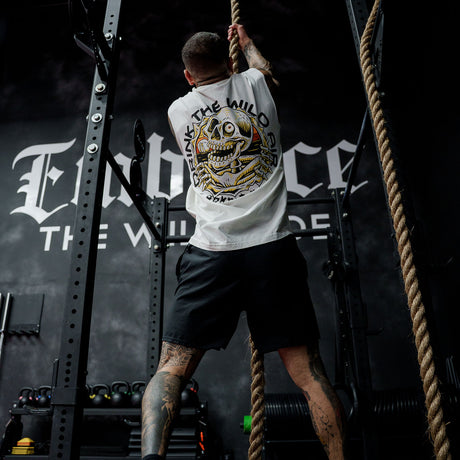 Male model rope climbing in gym wearing the sleeveless street tee with 'Drink The Wild Air' graphic
