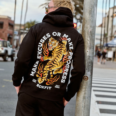 Male model outdoors wearing hoody with 'Make Excuses or Make Progress' graphic